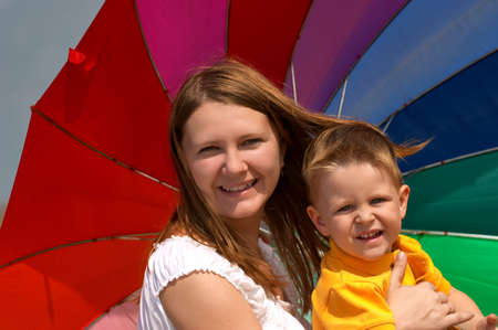 Happy young woman and kid under brightly colored umbrella having fun outdoors.の写真素材