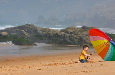Do not depend on weather conditions. Cute small boy with big brightly colored umbrella having fun on the beachの写真素材