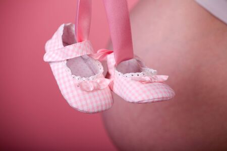 Pretty small pink shoes and pregnant belly on background