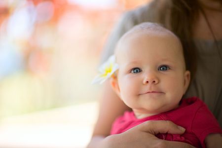 Portrait of cute 5 months old baby girl with tropical flower outdoor