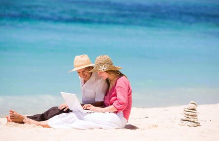 Looking for perfect vacation. Happy couple using laptop on the beach.の写真素材