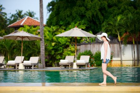 Beautiful girl walking along swimming pool at tropical resort
