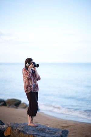 Beautiful young female photographer taking pictures on beach