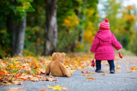 Cute 1 year old girl walking outdoors at autumn day. Focus on teddy bearの写真素材