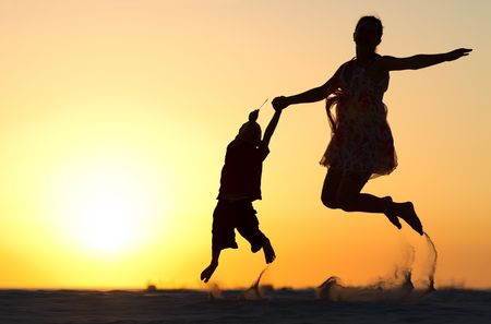 Mother and son silhouettes jumping on beach at sunsetの写真素材