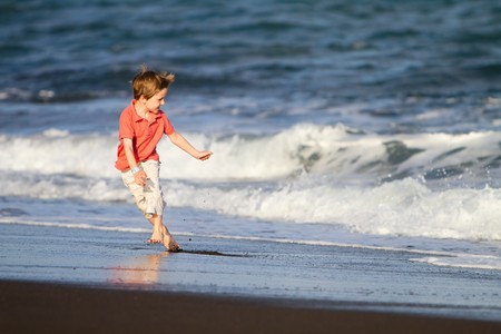 Boy running on black sand beach in Bali Indonesiaの写真素材