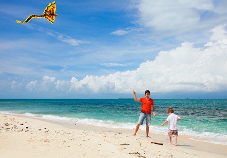 Young father and his son running with kite on the beachの写真素材