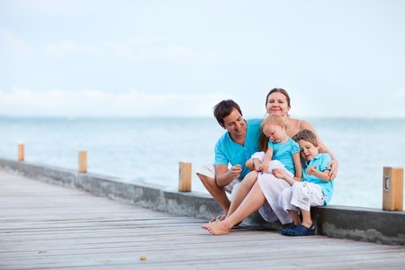 Family of four sitting on wooden jetty by the oceanの写真素材