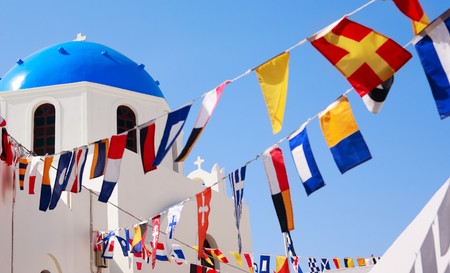 Classical Greek blue domed church and different flags in Oia village in Santorini, Greeceの写真素材