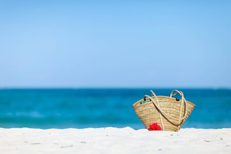 Photo of straw beach bag and red hibiscus flowers on exotic white sand beach with room for text and copyspaceの写真素材