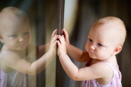 Outdoor casual portrait of adorable baby girl standing by glassed doorの写真素材