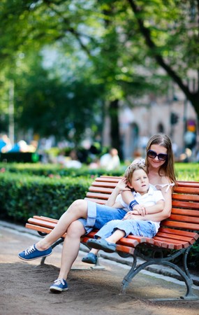 Young mother and her son sitting on bench in parkの写真素材