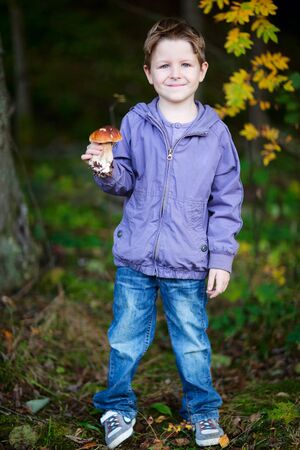 Full body portrait of cute boy with wild mushroom at forestの写真素材