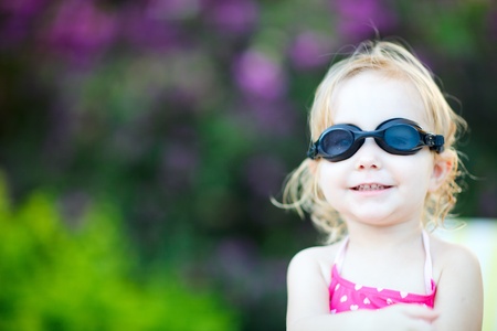 Adorable toddler girl in swimming glasses sitting near swimming poolの写真素材