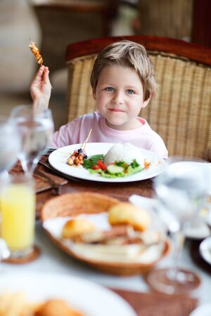 Cute boy having delicious lunch in restaurantの写真素材
