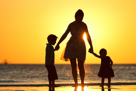 Mother and two kids silhouettes on beach at sunsetの写真素材