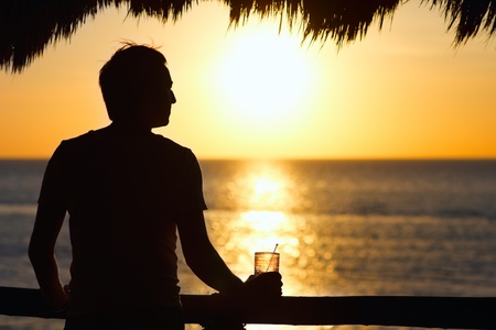 Silhouette of young man having drink at sunsetの写真素材
