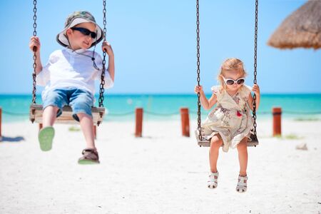 Little kids swinging with tropical beach on backgroundの写真素材