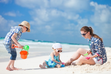 Mother and two kids playing with sand on tropical beachの写真素材