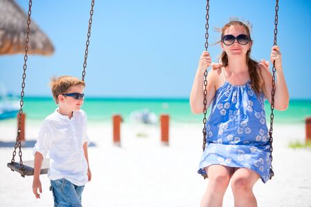 Mother and son swinging with tropical beach on backgroundの写真素材