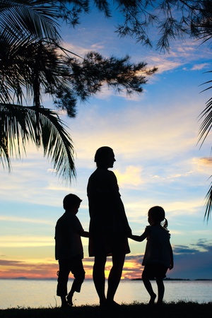 Silhouettes of mother and two kids at sunsetの写真素材