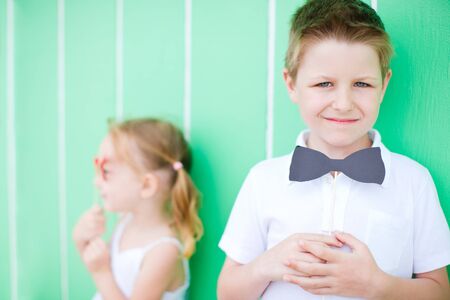 Portrait of cute boy over colorful background holding bow tie party accessoryの写真素材