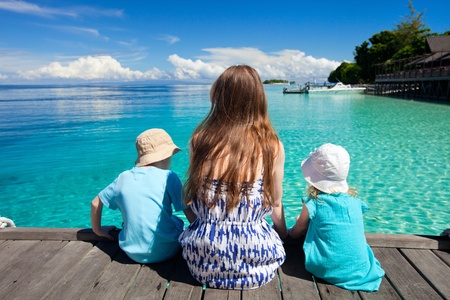 Back view of mother and kids sitting on wooden dockの写真素材