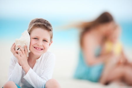 Cute boy with seashell at the beach with his family on backgroundの写真素材