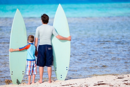 Back view of father and son with surfboards at beachの写真素材