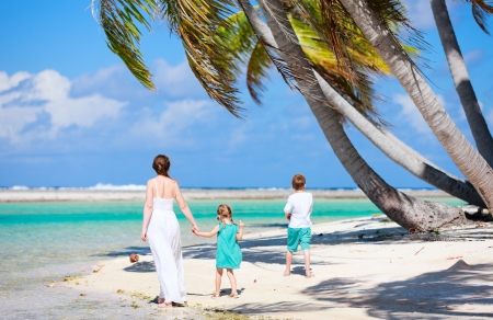 Back view of a mother walking with her two kids along a tropical beachの写真素材