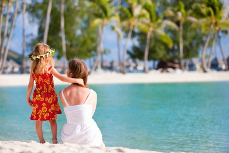 Back view of mother and daughter wearing Polynesian dress on a tropical beachの写真素材