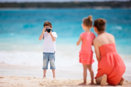 Boy photographing his mother and little sister at tropical beachの写真素材