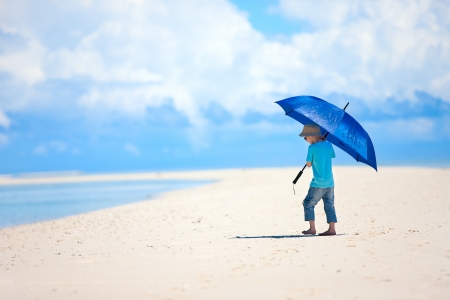 Little boy with umbrella walking along tropical beachの写真素材