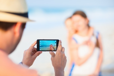 Young man making photo of his wife and daughter at tropical beach. Focus on cameraの写真素材