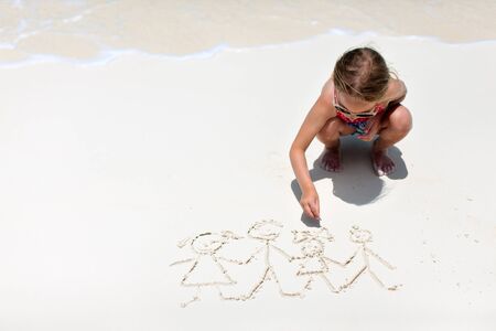 Little girl drawing family picture on a beachの写真素材