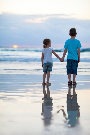 Brother and sister on beach at sunsetの写真素材