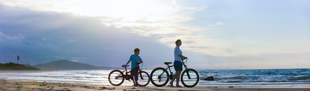 Panorama of mother and son biking on a beach at sunsetの写真素材