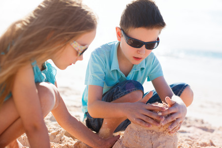 Brother and sister playing with sand at tropical beachの写真素材