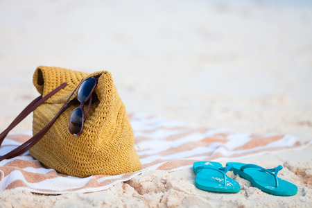 Straw bag, sun glasses, towel and flip flops on a tropical beach の写真素材
