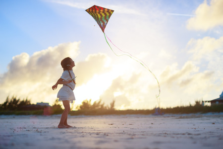 Little girl flying a kite on beach at sunsetの写真素材