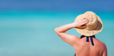 Back view of a young beautiful woman in straw hat at tropical beachの写真素材
