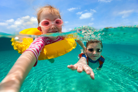 Split above and underwater photo of adorable kids having fun swimming on summer vacationの写真素材