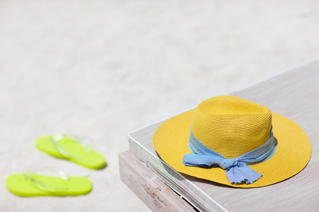 Yellow hat on a lounge chair and flip flops at tropical beachの写真素材