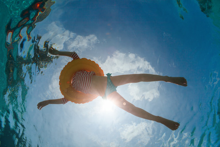Underwater photo of a little girl swimming with inflatable ring in poolの写真素材