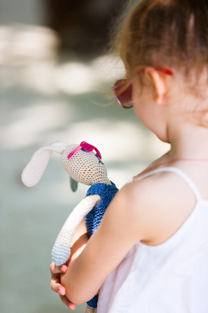 Little girl with her favorite knitted bunny toy both wearing pink sunglasses outdoors on summer dayの写真素材
