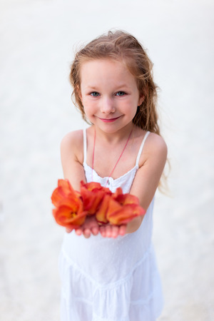 Adorable little girl in a white dress holding red tropical flowersの写真素材