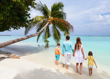Back view of a beautiful family standing on a tropical beach with palm tree during summer vacationの写真素材