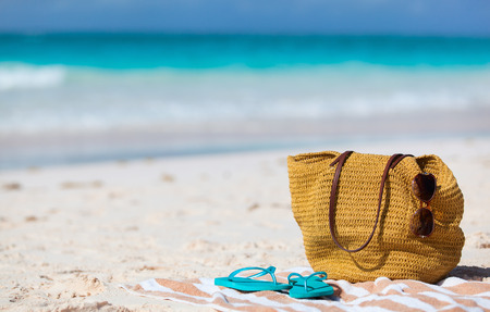 Beach vacation close up. Straw bag, sun glasses, towel and flip flops on a tropical beach の写真素材