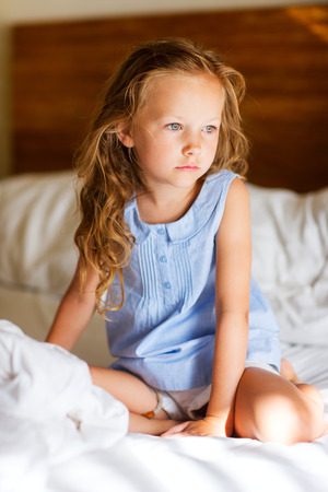 Sweet little girl with curly hair in light blue pajama sitting on bedの写真素材