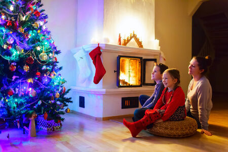 Mother and her two little kids sitting by a fireplace in their family home on Christmas eveの写真素材